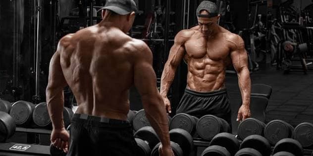 Athlete standing at a dumbbell rack in front of a gym mirror